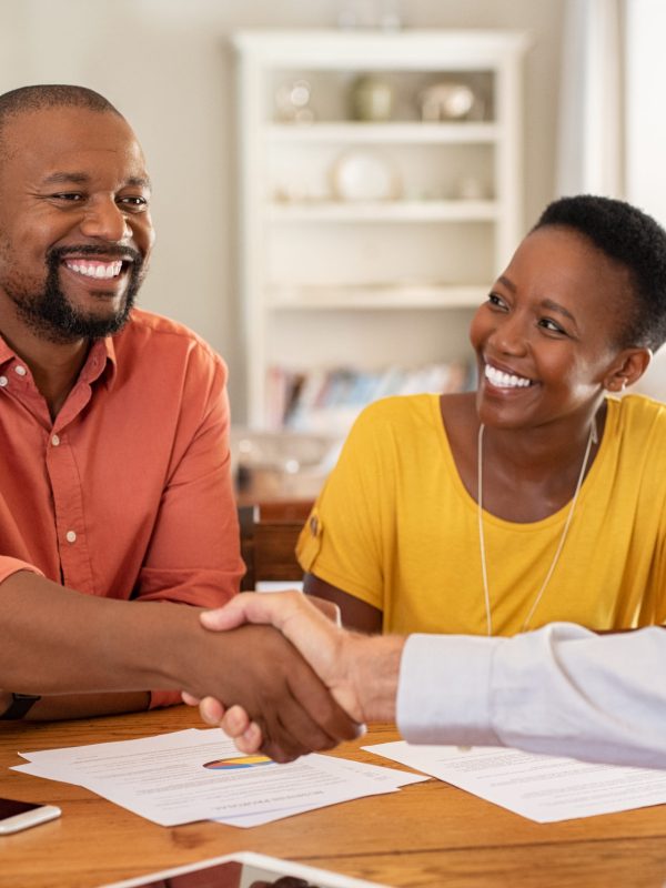 Mature black husband shaking hands with senior agent on taking loan. Happy african couple sealing with handshake a contract with financial advisor for investment. Man making sale purchase deal concluding with a handshake with estate agent.